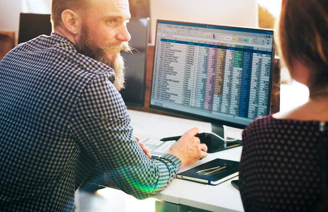 Caucasian man using computer talking with colleague